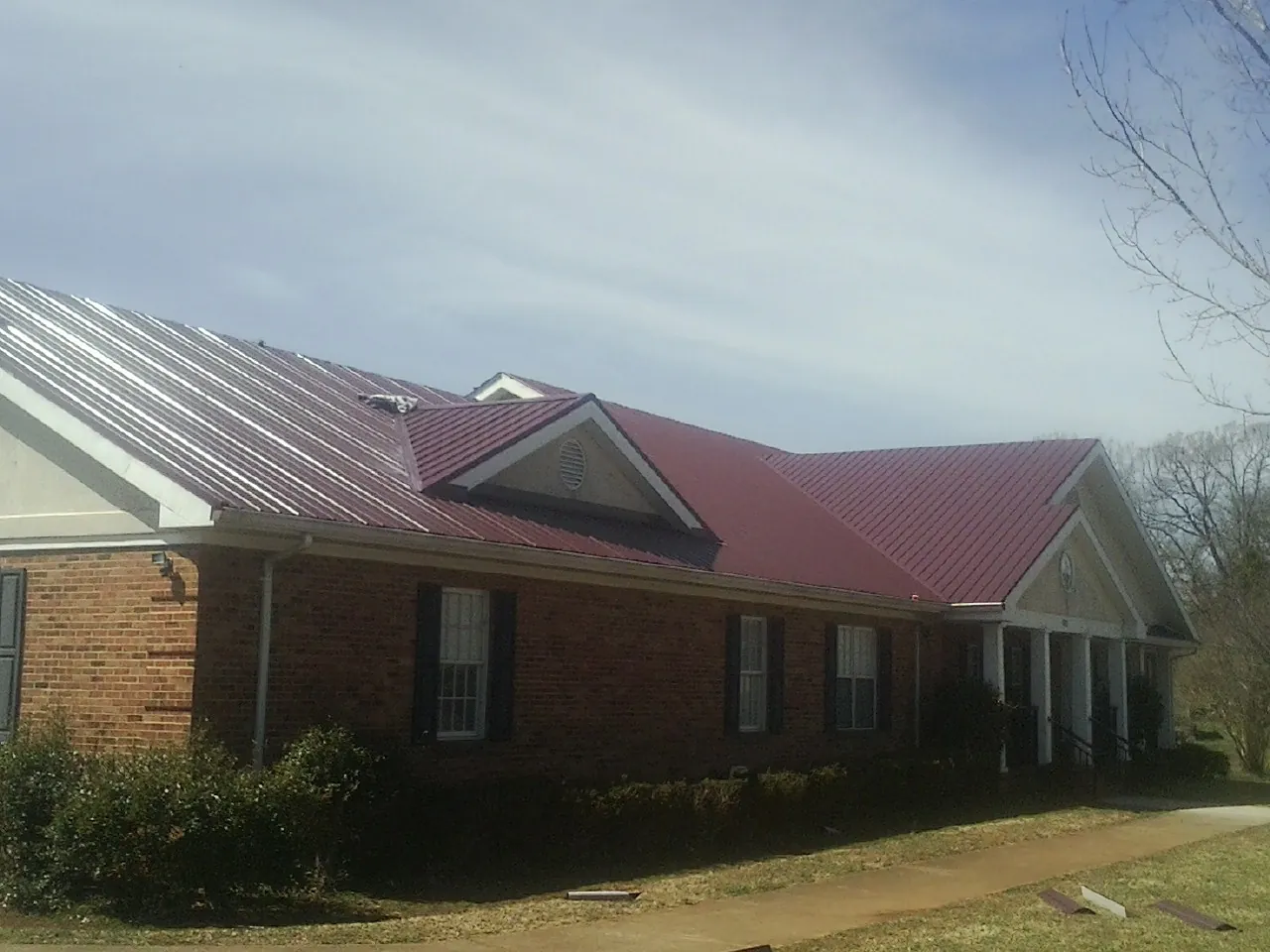Red metal roof with gabled entries on a long brick building, from a Hail Damage Roof Repair job in Newmanstown