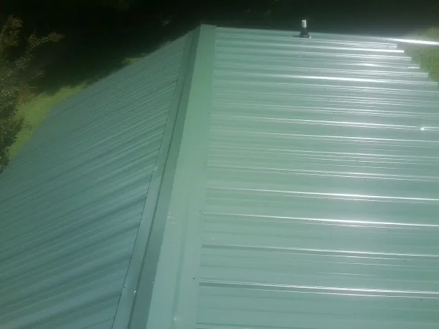 New green metal panels meeting at the ridge of a roof — Flat Roof Repair work by our crew in Newmanstown