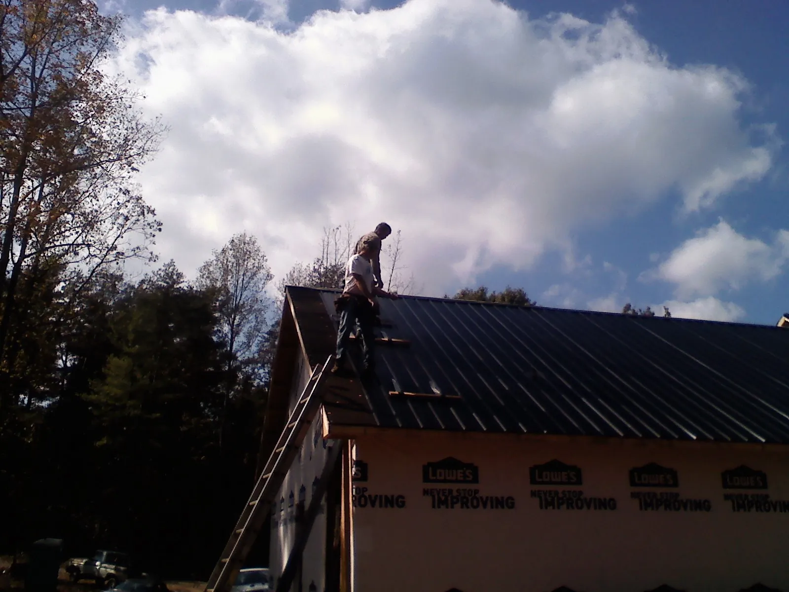 Roofer fastening dark metal panels high against a cloudy sky, from a Roof Inspection job in Newmanstown