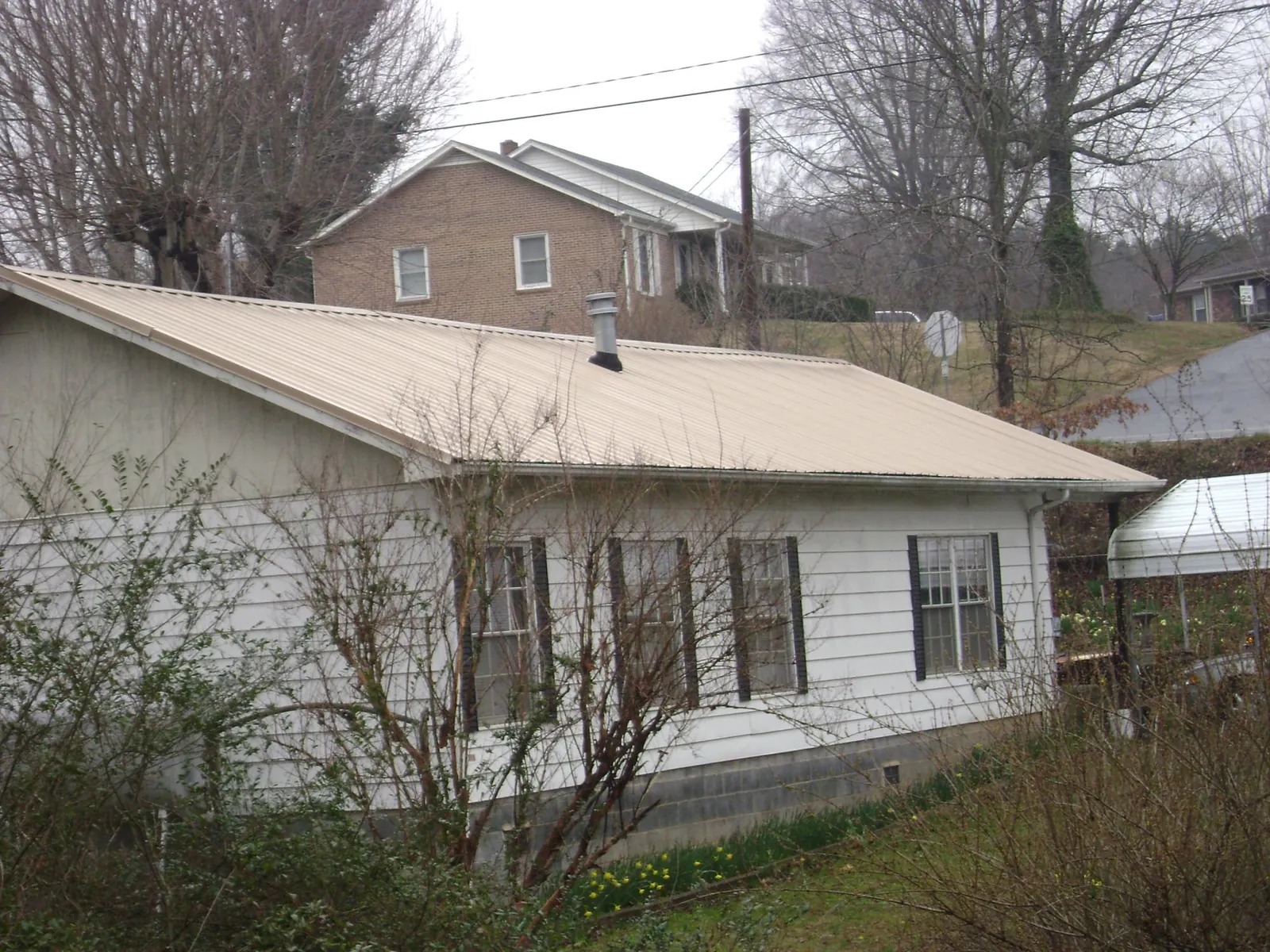 Tan metal roof on a white sided house set into a hillside — Commercial Roofing by Roofing Brothers in Newmanstown